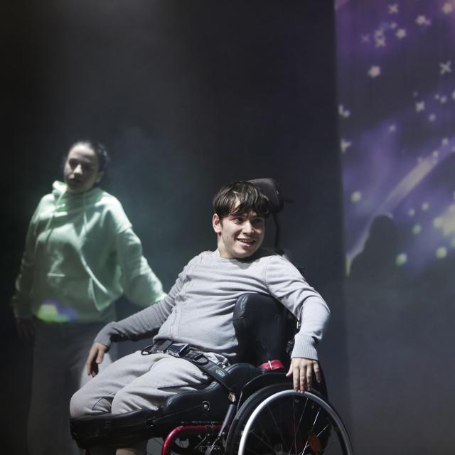 Un jeune homme en fauteuil roulant souriant sur scène