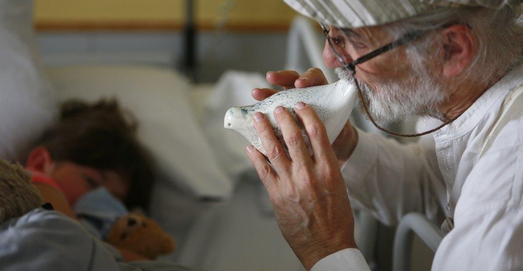 Un homme soufflant dans un petit instrument en forme d'oiseau à côté d'un enfant allongé dans un lit