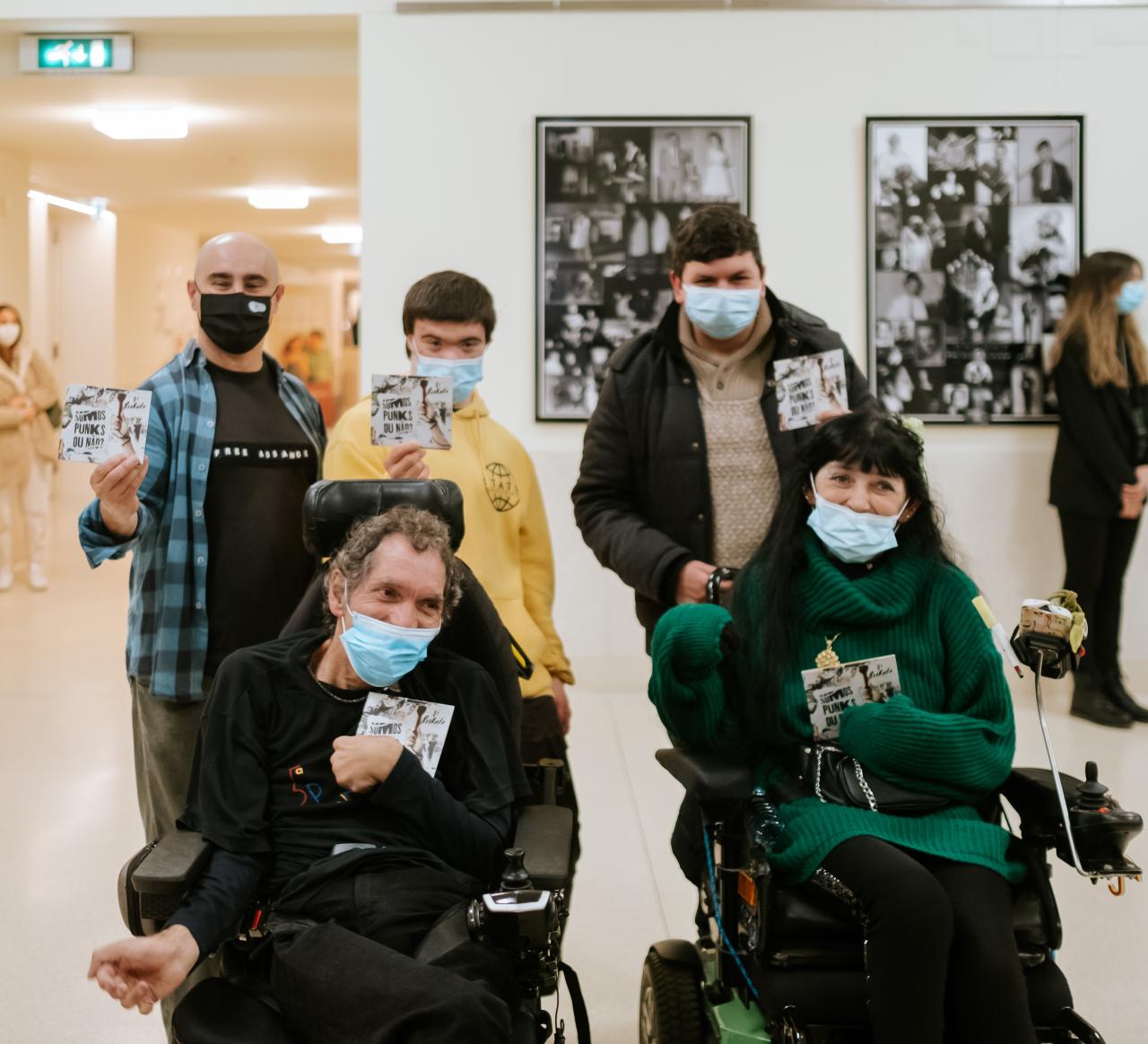 Deux personnes en fauteuil roulant et trois autres personnes debout derrière eux avec un album dans la main