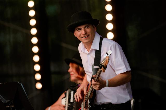 Un homme souriant avec un chapeau qui joue de la guitare