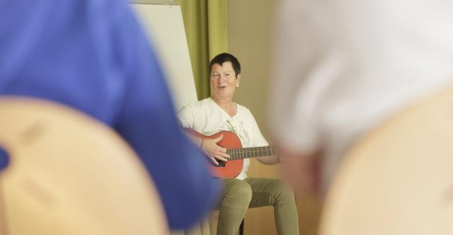 Un femme qui chante assise avec sa guitare, devant un public