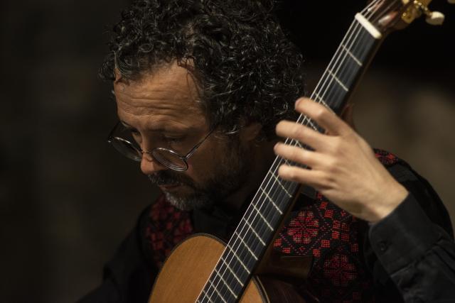 A man leans over his guitar and plays