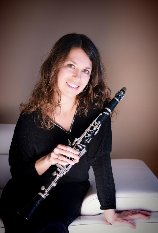 A woman smiling from the front with a clarinet in her hand