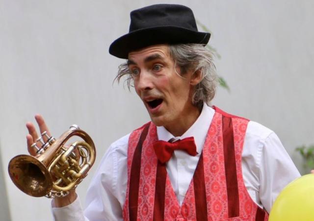 A man dressed as a clown sings with a trumpet in his hand