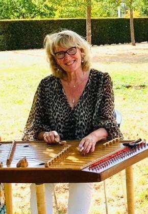 A smiling woman seated in front playing a cymbalum