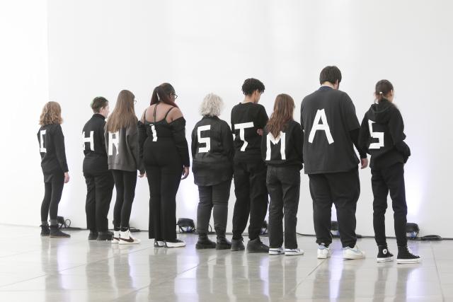 Des adolescent habillés en noir et de dos avec une lettres sur leur t-shirt formant le mot "christmas"