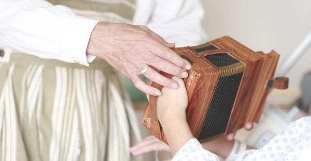 Un homme aidant un enfant hospitalisé à jouer d'un instrument en forme d'accordéon