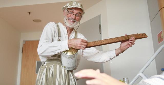 Un homme qui joue un instrument ressemblant à une guitare à côté d'un lit d'hôpital