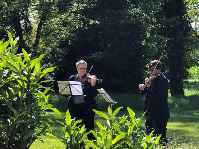 2 hommes dans un jardin jouant du violon