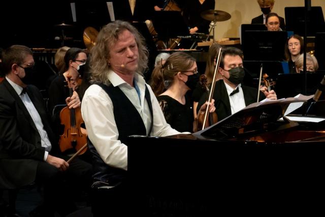 Un homme jouant du piano et derrière lui un orchestre