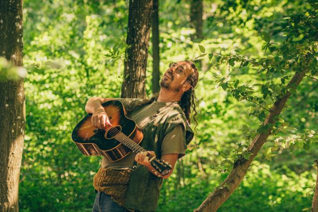 A man plays guitar in the forest