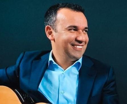 A seated man smiling and playing the guitar