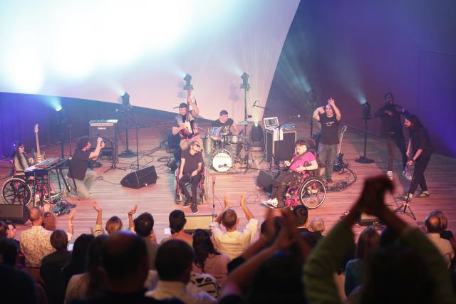 Des musiciens à besoins spécifiques sur scène devant un public debout