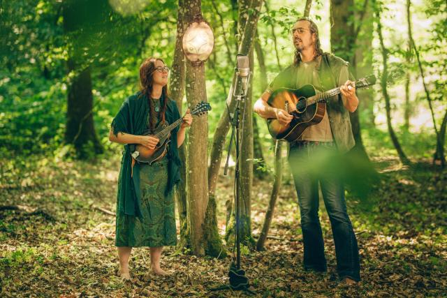 A man playing the guitar and a woman playing the mandolin in the forest