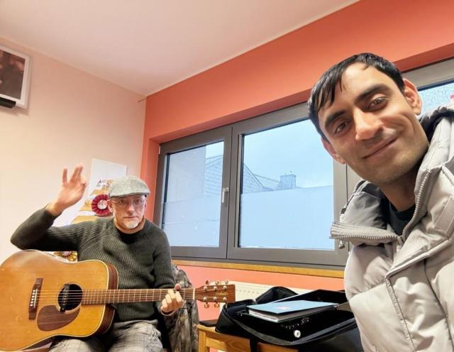 A man with a guitar and another smiling beside him